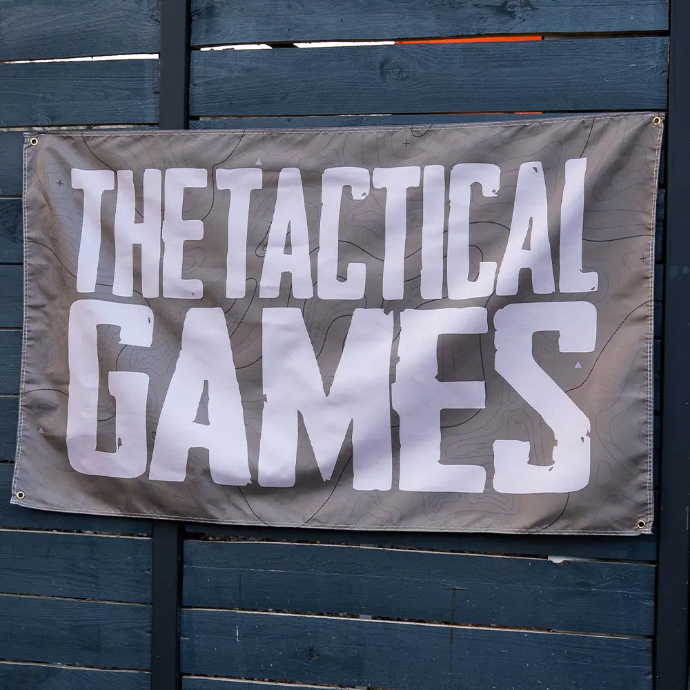 A rectangular gray horizontal  banner with the words 'THE TACTICAL GAMES' in large white block letters, 